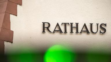 Foto: Das Wort "Rathaus" - einzelne Metallbuchstaben - an einer Hauswand. Am seitlichen Rand ist etwas Sandstein zu sehen. Am vorderen Rand ein grüner Lichtfleck, vermutlich von der Kamera.