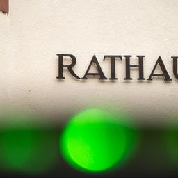 Foto: Das Wort "Rathaus" - einzelne Metallbuchstaben - an einer Hauswand. Am seitlichen Rand ist etwas Sandstein zu sehen. Am vorderen Rand ein grüner Lichtfleck, vermutlich von der Kamera.