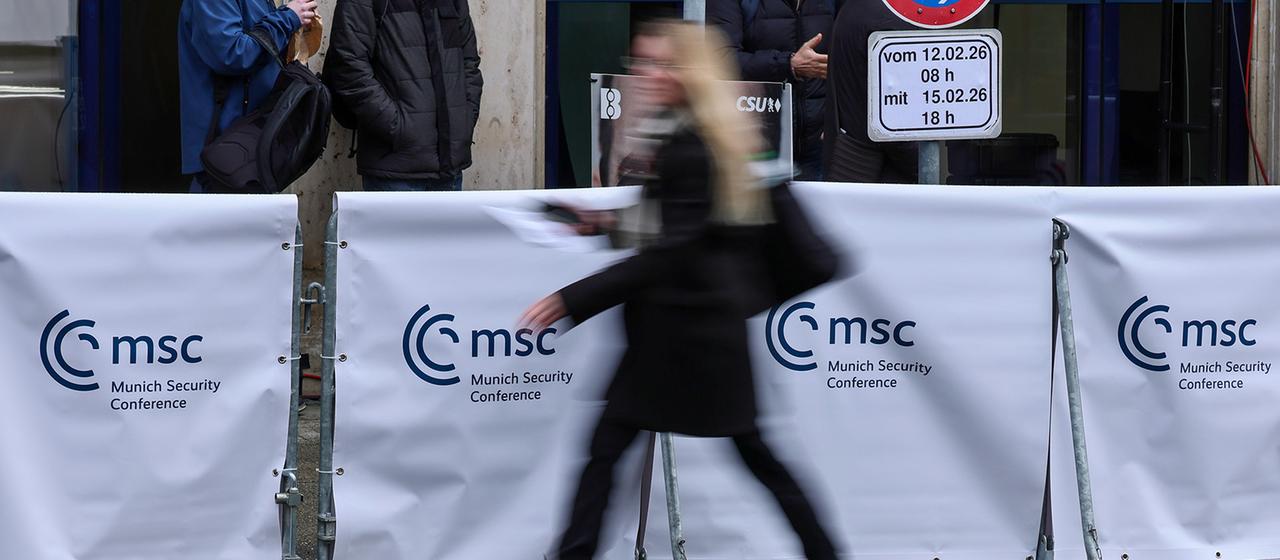 Eine Frau geht an einem Absperrung mit dem Logo der Münchner Sicherheitskonferenz vorbei.
