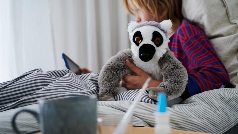 Ein krankes Kind liegt mit Kuscheltier im Bett.