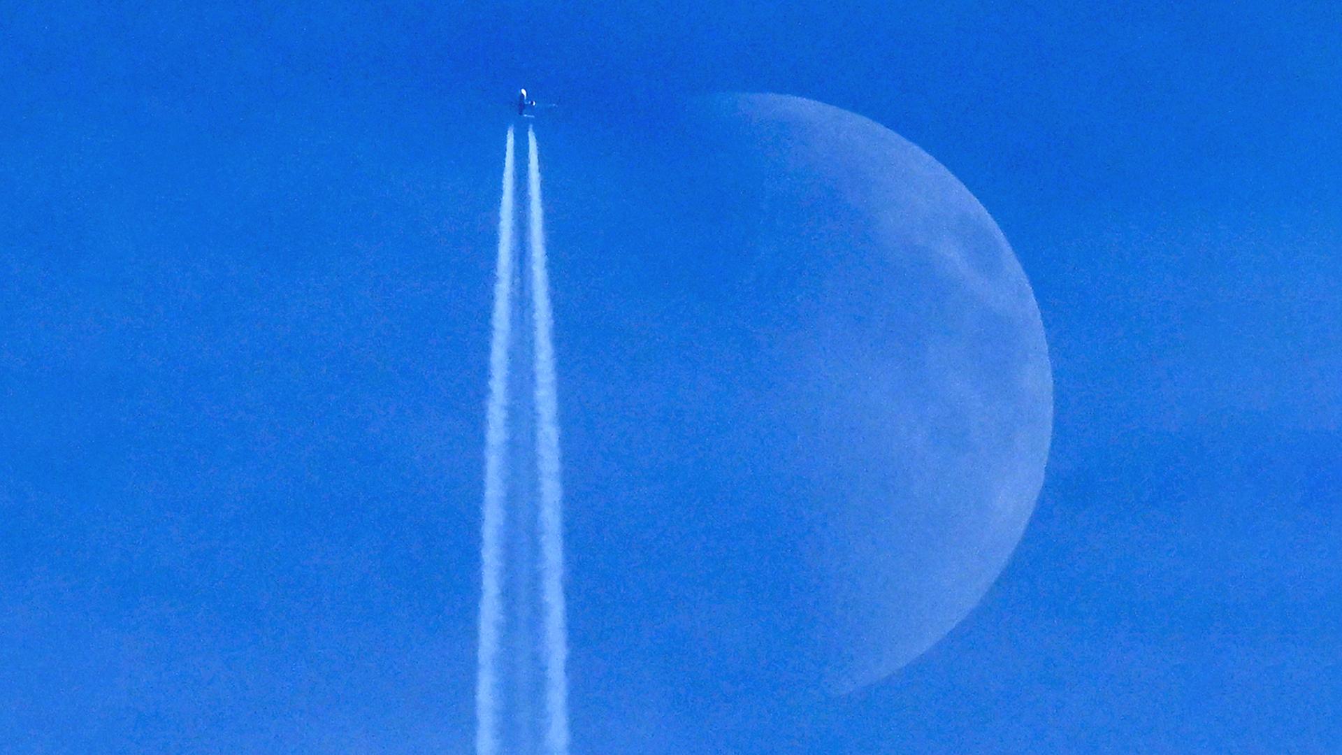 Ein Flugzeug fliegt vor dem Mond an blauem Himmel vorbei. | AFP
