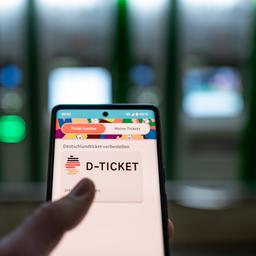 Ein Fahrgast hält ein Smartphone mit einem digitalen Deutschlandticket an einer U-Bahnstation in der Hand.