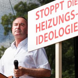 Hubert Aiwanger steht auf einer Bühne neben einem Schild mit der Aufschrift "Stoppt die Heizungsideologie"