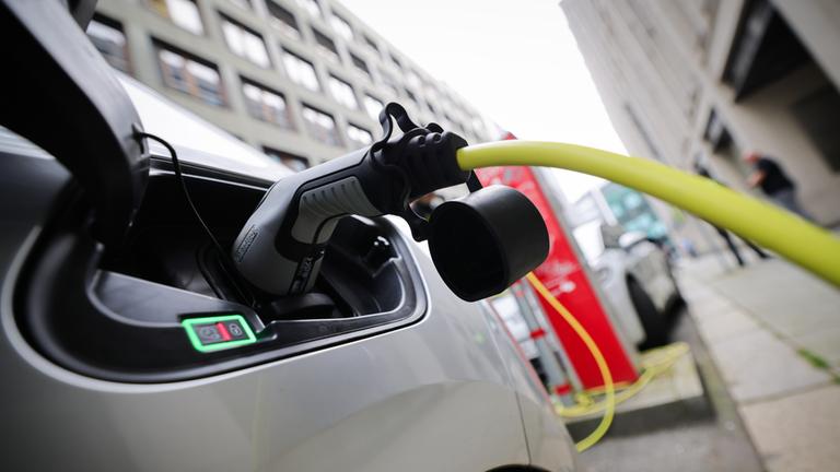 Ein silbernes E-Auto steckt an einer Ladesäule