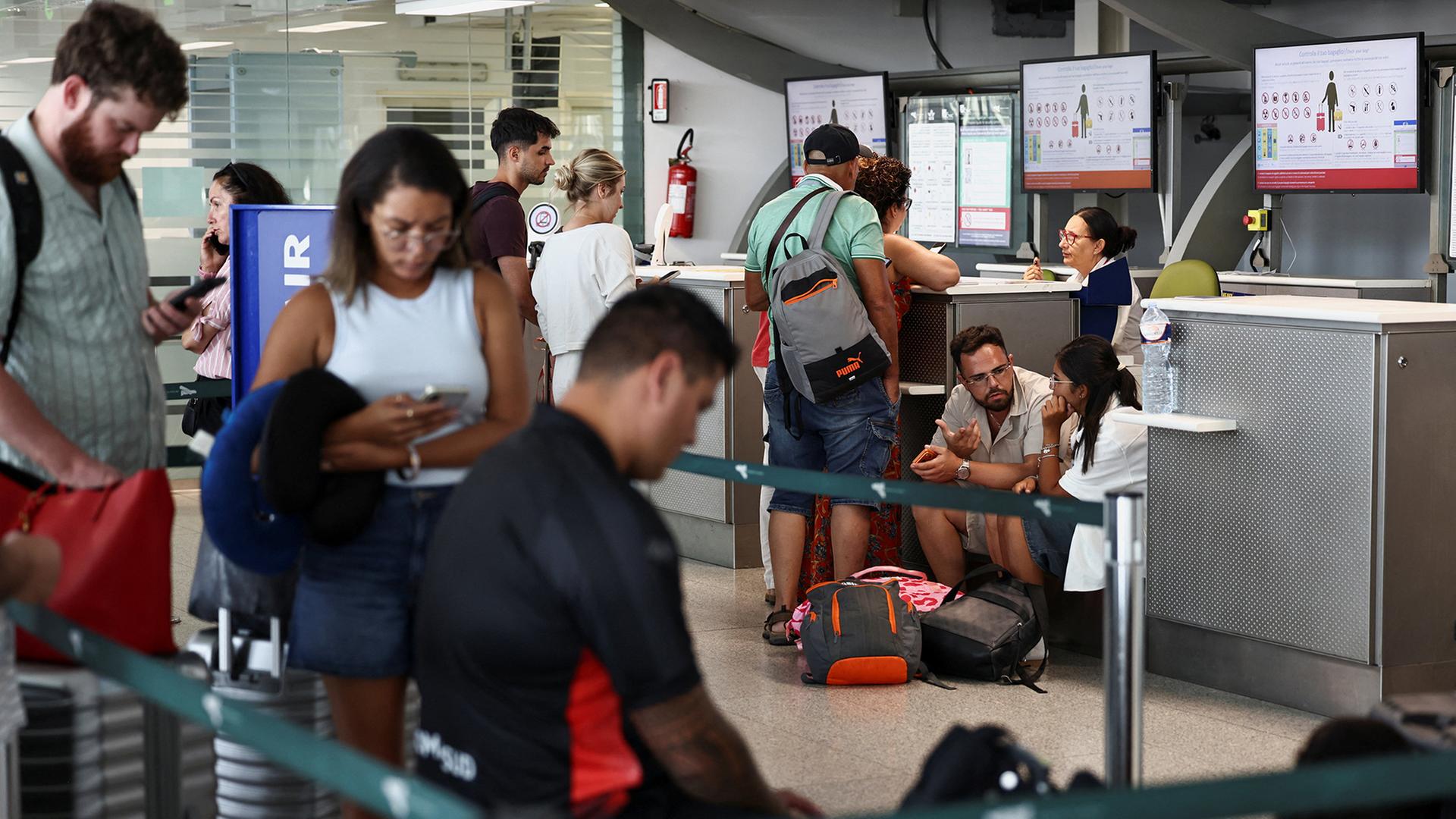 Menschen warten vor einem Schalter eines Flughafenterminals. | REUTERS
