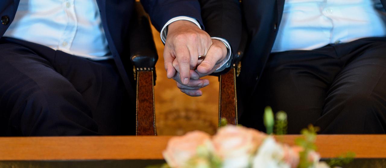 Zwei Männer halten sich bei der Eheschließung die Hände.