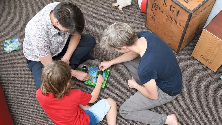 Ein verheiratetes lesbisches Paar spielt mit seinem Sohn ein Spiel.