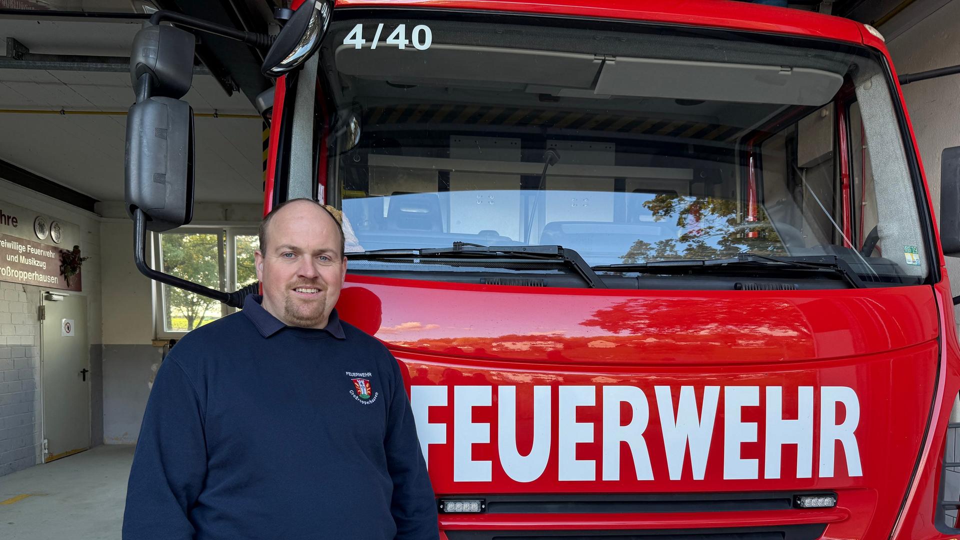 Ein Mann steht vor einem Feuerwehrauto. Das Fahrzeug steht in einer Halle. | Kübra Anac (hr)