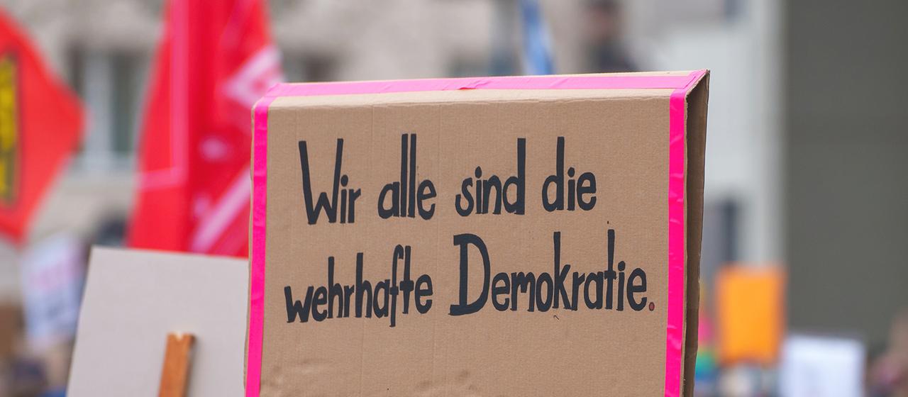 "Wir alle sind die wehrhafte Demokratie" steht auf einem Plakat bei der Kundgebung in Offenbach.