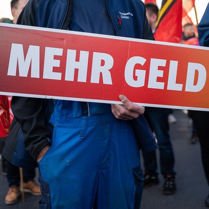 Ein Teilnehmer eines Warnstreiks hält ein Plakat mit der Aufschrift "Mehr Geld"