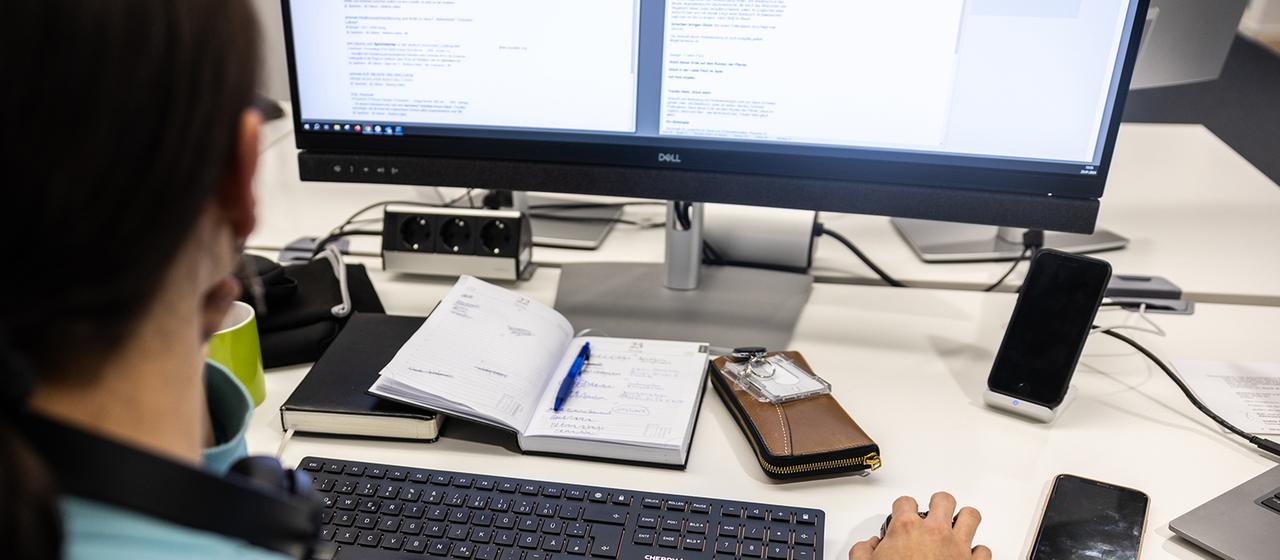 Eine Frau sitzt am Schreibtisch und arbeitet am Computer.