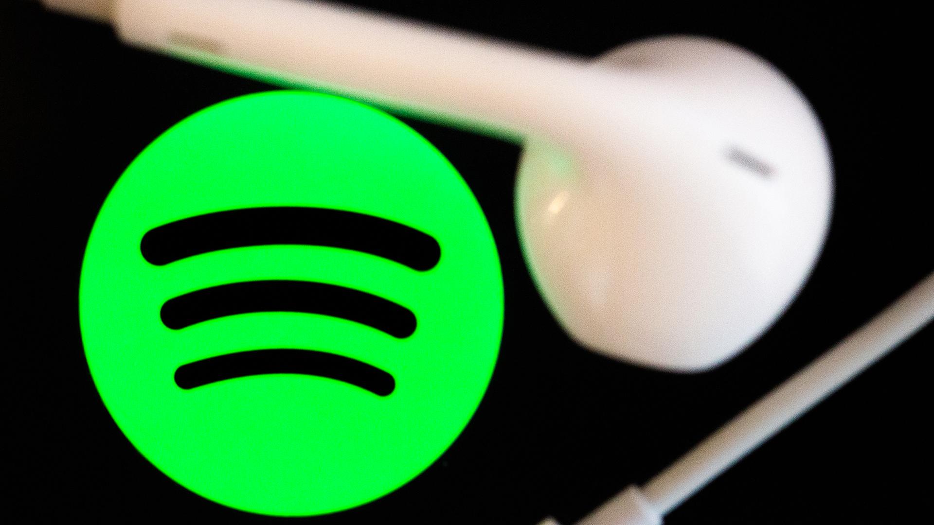  Kopfhörer liegen auf dem Bildschirm eines Smartphones, auf dem das Logo vom Musikstreaming-Dienst Spotify angezeigt wird. | dpa