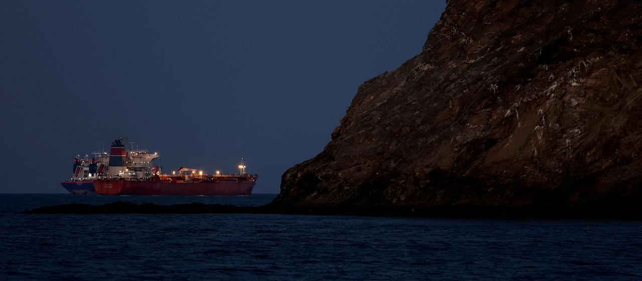Ein beleuchteter Öltanker ankert vor einem Felsen.