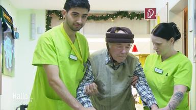 Eine kolumbianische und eine deutsche Pflegekraft stützen einen dementen Rentner.