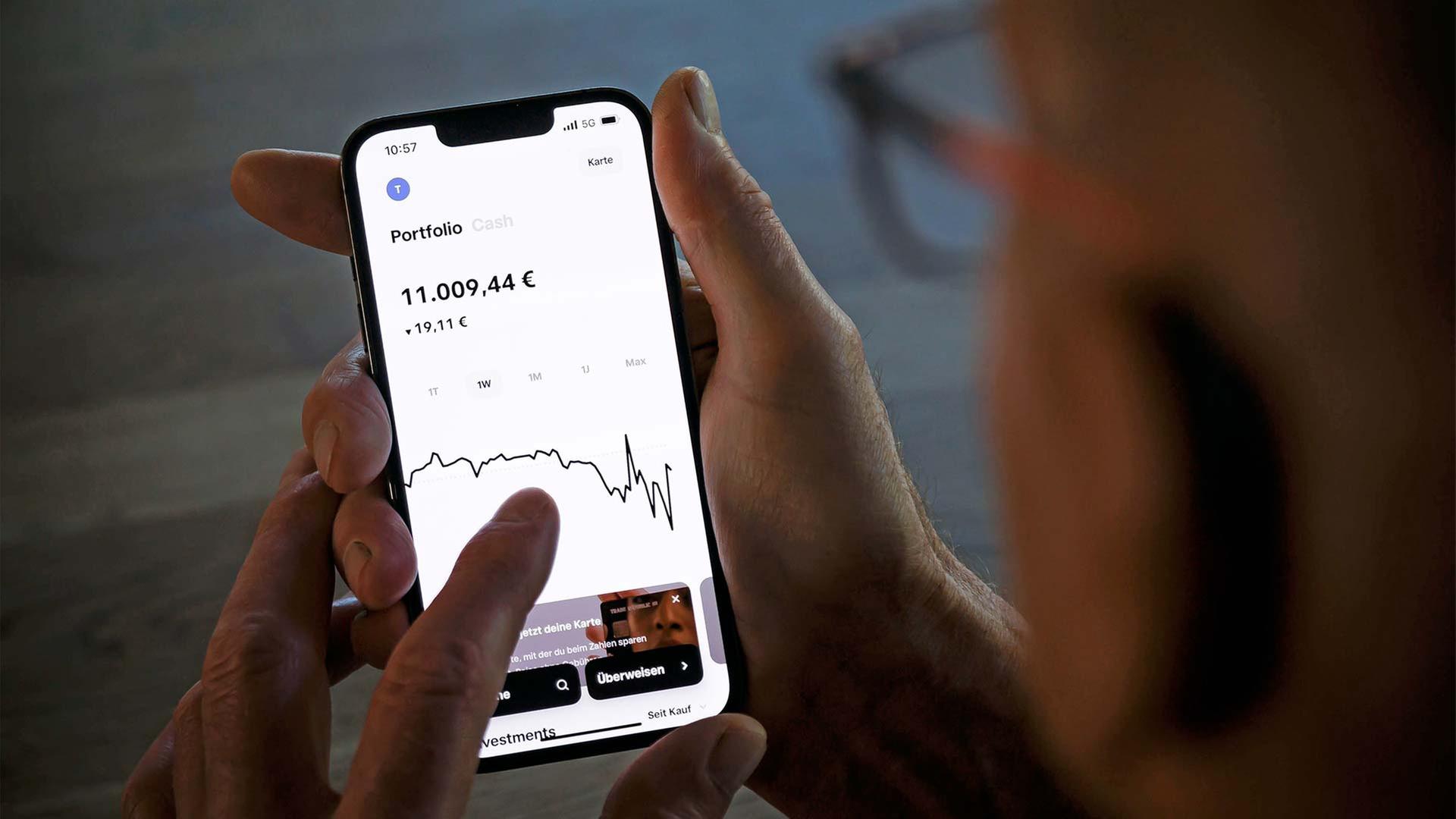 Ein Alter Mann hält ein Smartphone und prüft den Kurs seiner Geldanlage. | picture alliance / photothek.de