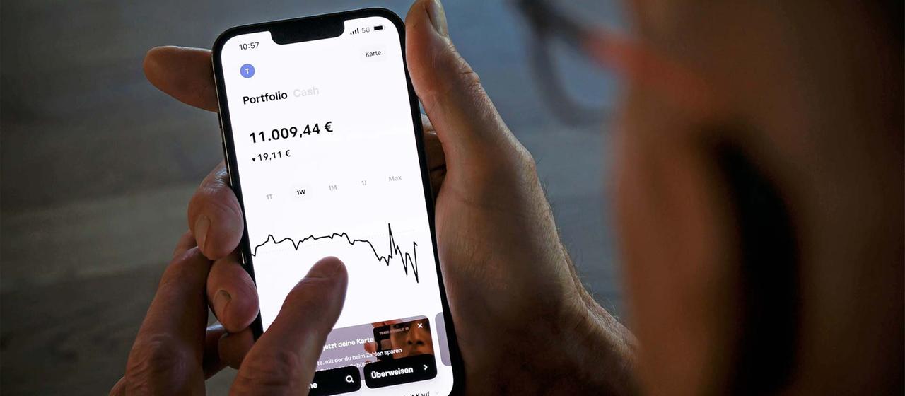 Ein Alter Mann hält ein Smartphone und prüft den Kurs seiner Geldanlage.