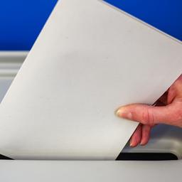 Eine Hand steckt einen Wahlzettel in eine Wahlurne.