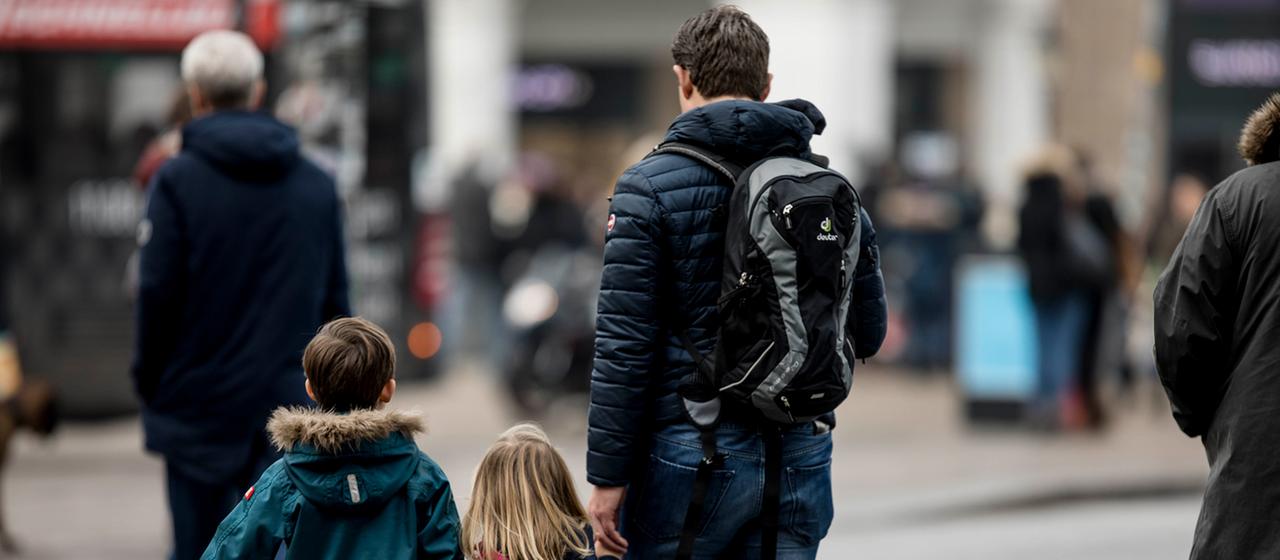 Ein Vater geht mit seinen Kinder über eine Straße.