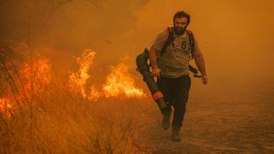 Ein Mann läuft mit einem Feuerlöscher durch eine brennende Landschaft.