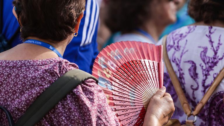 Eine Touristin wedelt sich bei heißem Sommerwetter mit einem Fächer Luft zu.