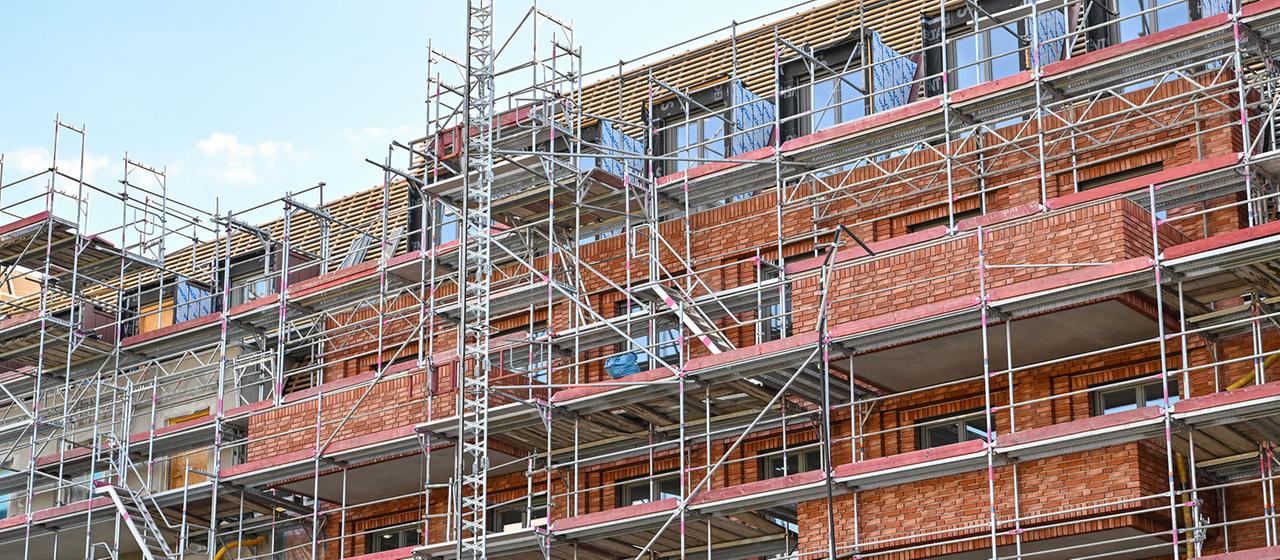 Eine Baustelle eines Mehrfamilienhauses ist eingerüstet.