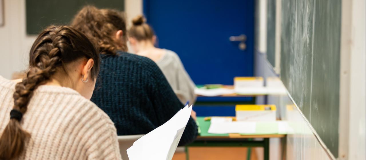 Schülerinnen und Schüler sitzen während einer Prüfung in einem Klassenzimmer in einem Gymnasium.