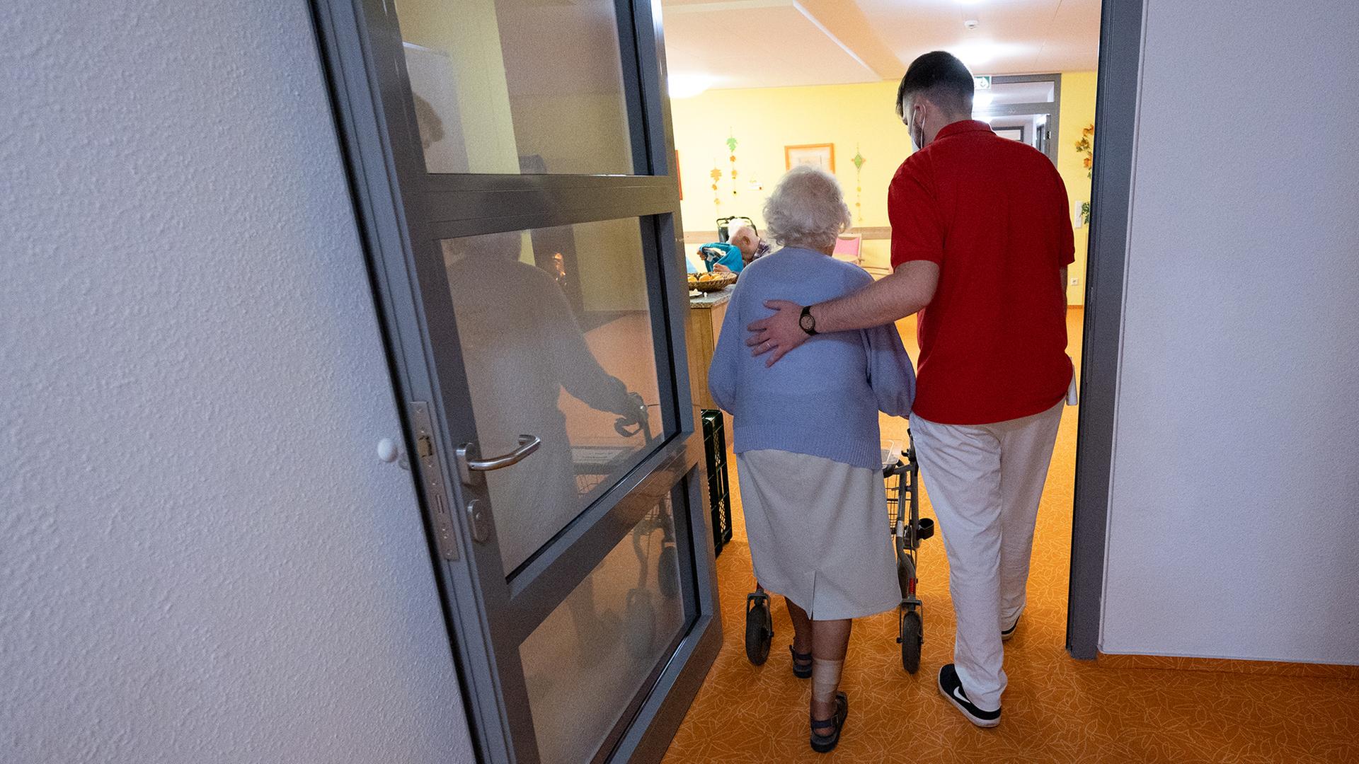 Ein Pfleger begleitet eine ältere Frau in einem Altenheim. | dpa
