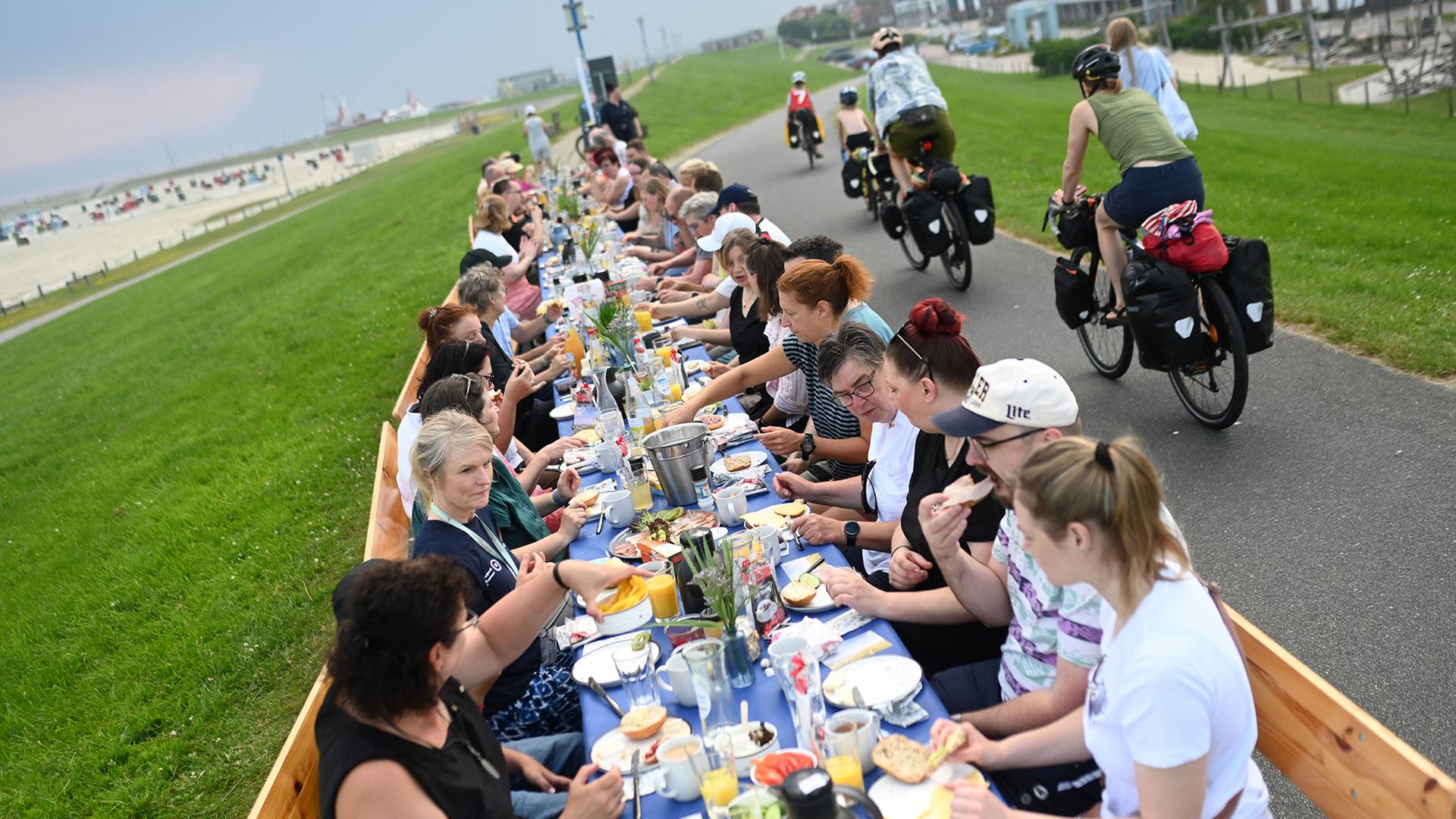Zahlreiche Menschen frÃ¼hstÃ¼cken an einer langen Tafel auf einem Deich. | Lars Penning/dpa