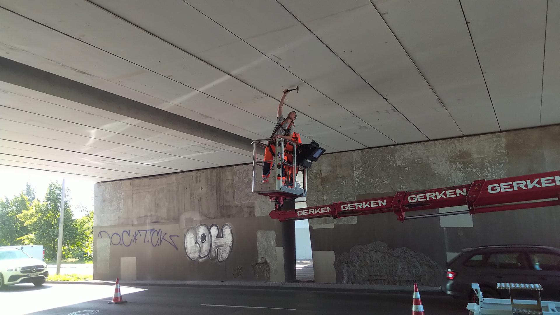 Ein Arbeiter klopft mit einem Werkzeug an einer Brücke. | Andre Kartschall