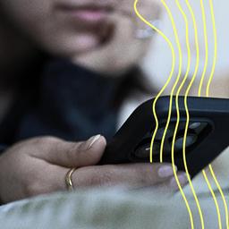 Eine junge Frau liegt mit dem Smartphone in der Hand auf dem Bett.