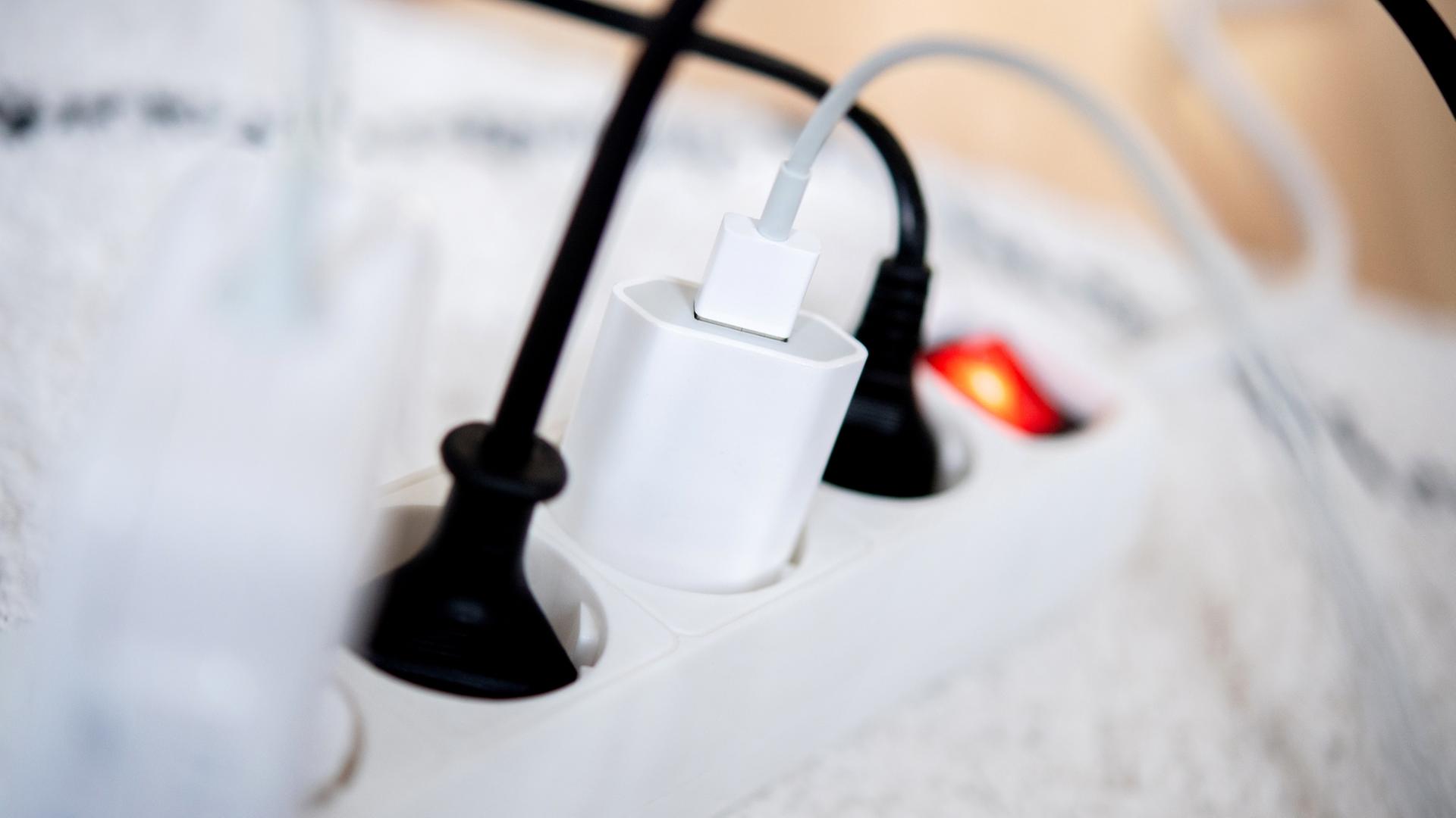 Die Netzstecker mehrerer Elektrogeräte stecken in einer Steckdosenleiste in einem Wohnzimmer. | dpa