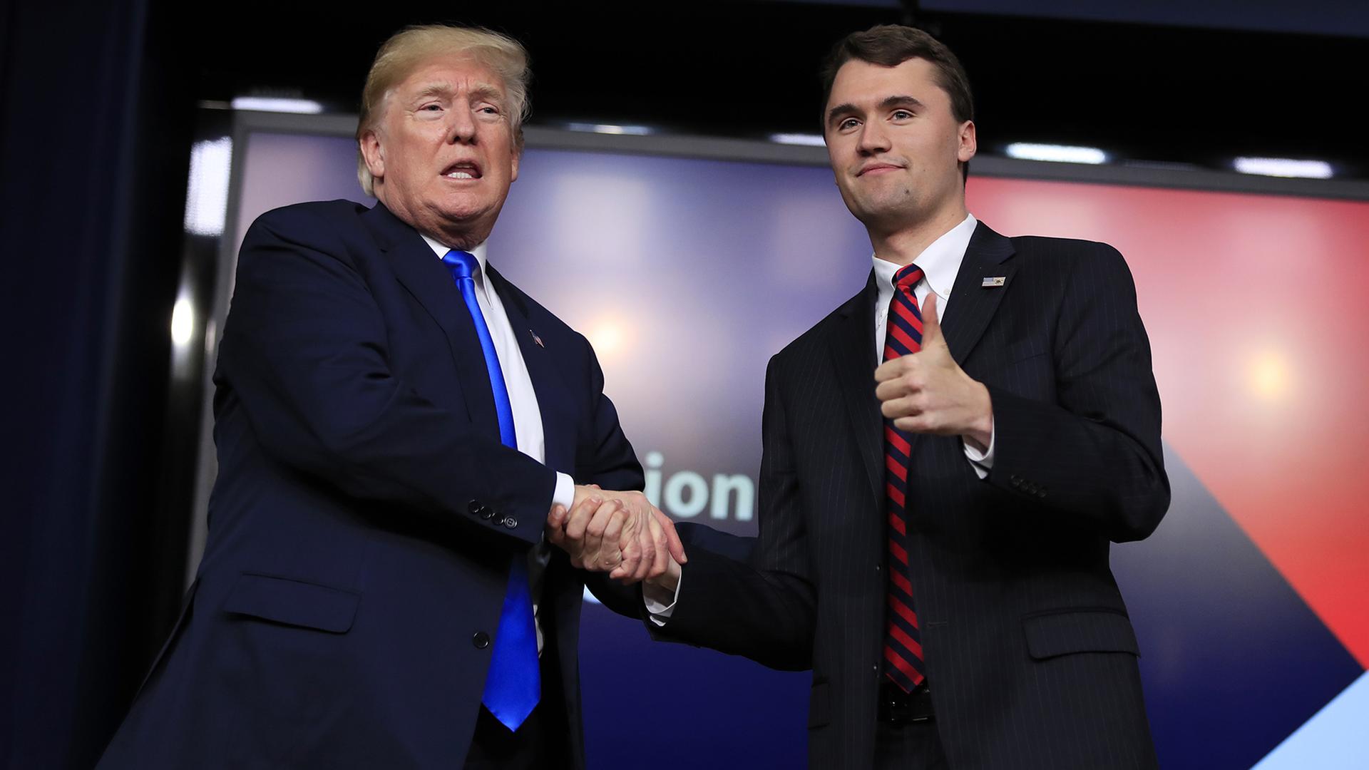 Donald Trump und Charlie Kirk geben sich auf einer Bühne die Hand. (Archivbild: 22.03.2018,) | dpa