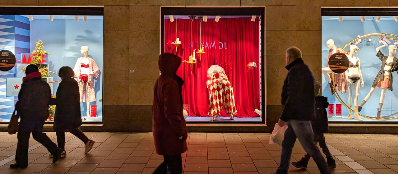 Passanten in München laufen an einem beleuchtetem Schaufenster vorbei.