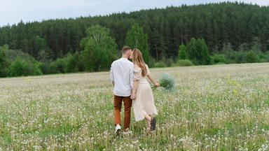 Ein junges Paar küsst sich auf einem Feld mit Blumen.