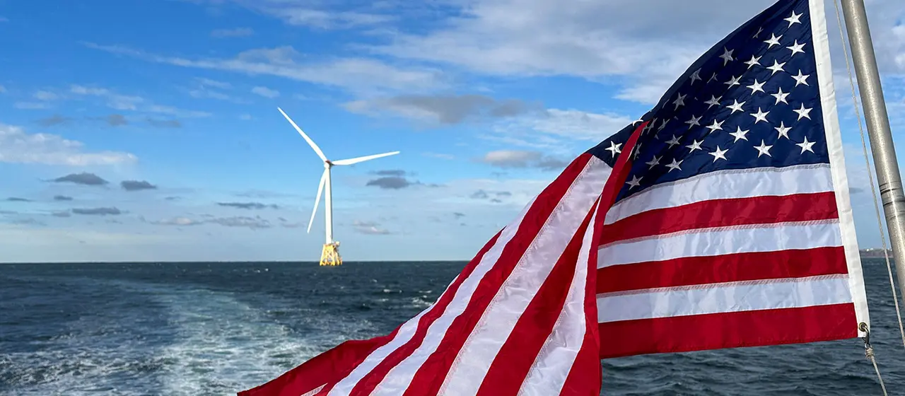 Ein Windrad auf dem Meer, im Vordergrund eine USA-Flagge.