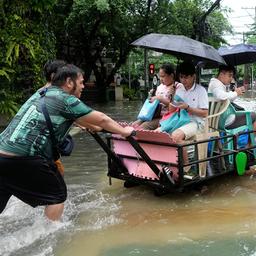 Männer schieben einen Karren mit Menschen entlang einer überfluteten Straße.