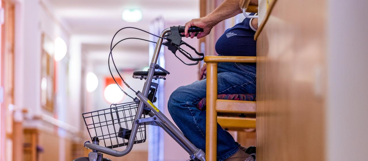Ein Bewohner sitzt mit seinem Rollator im Flur eines Pflegeheims