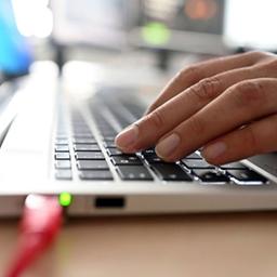 Eine Hand tippt auf der Tastatur eines Laptops.