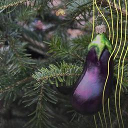 Eine Christbaumkugel in Form einer Aubergine hängt an einem Tannenbaum.
