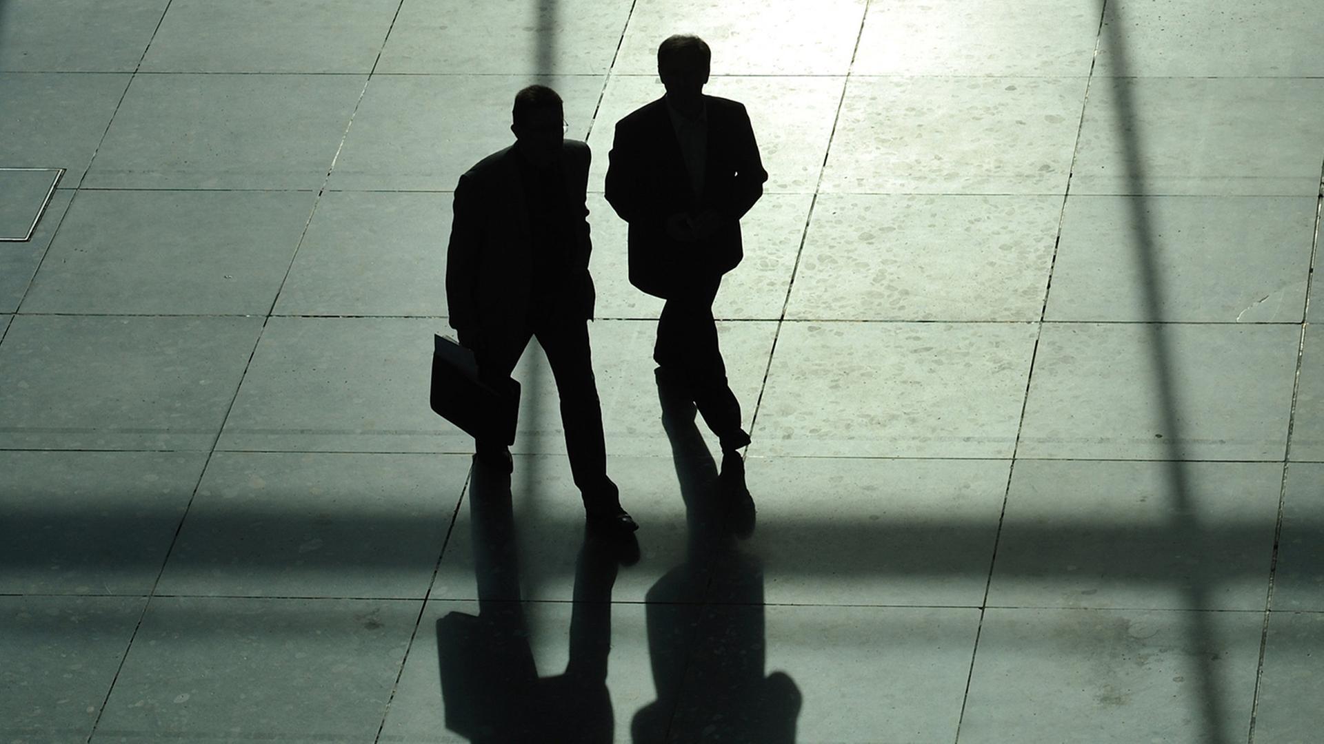 Die Schatten zweier Männer mit Anzug und Koffer. | dpa