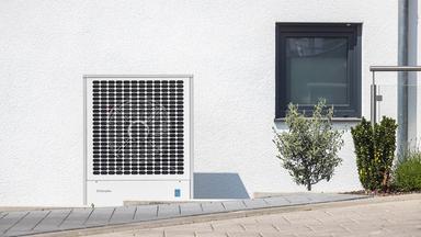Eine Wärmepumpe steht vor einem neuen Wohnhaus.