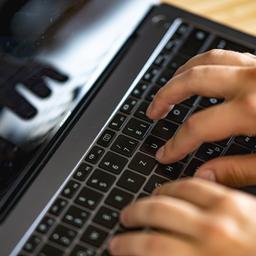 Ein Mann tippt auf einer Tastatur eines Laptops.