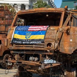 Ausgebrannte russische Militärfahrzeuge in Kiew, darauf ein Banner mit der Aufschrift: "Ich stehe an der Seite der Ukraine" mit der ukrainischen und US-amerikanischen Flagge.