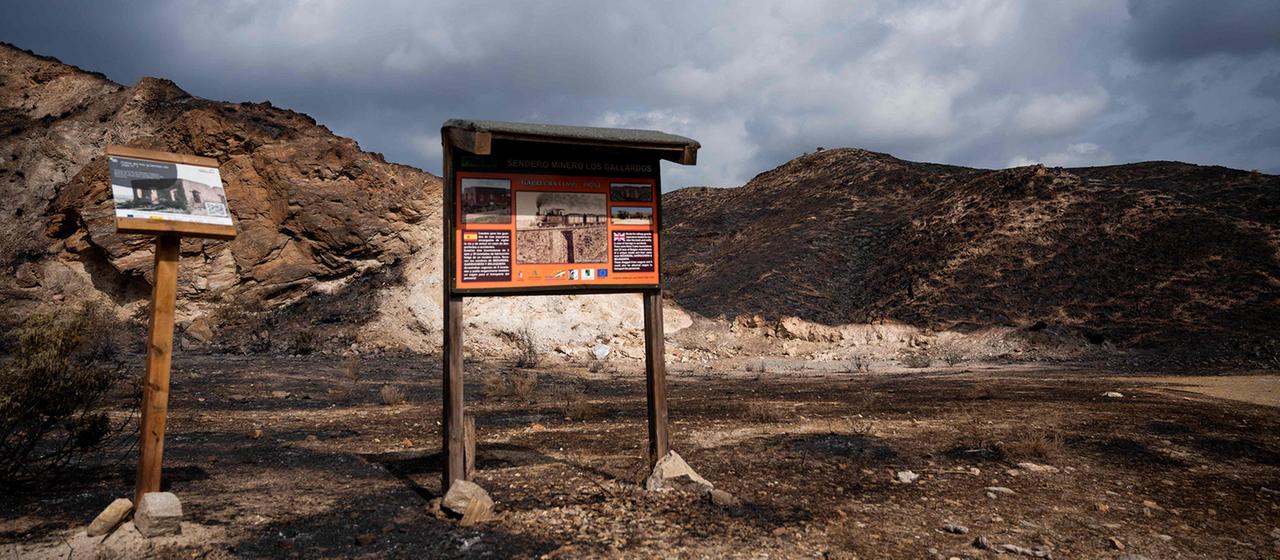 Informationstafeln zu historischen Bergbaupfaden sind inmitten einer verbrannten Landschaft zu sehen.