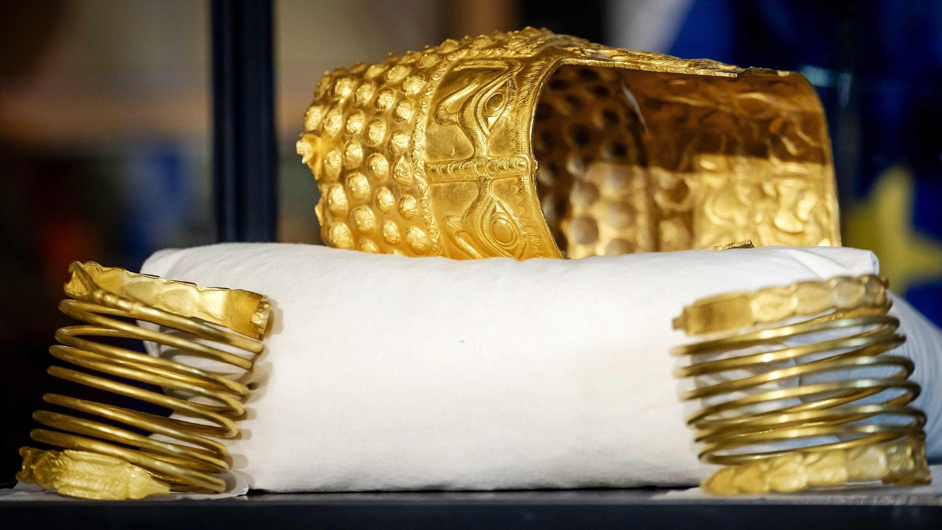Zwei goldene Armreifen und ein verzierter goldener Helm liegen auf einem weißen Kissen. | Sem Van Der Wal/ANP/dpa
