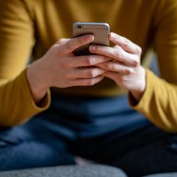 Eine junge Frau hält ein Smartphone in der Hand.