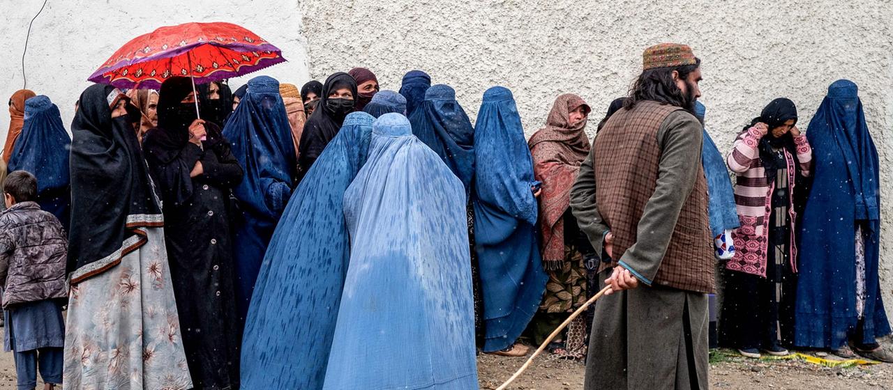 Ein Angehöriger der Taliban steht Wache, während afghanische Frauen in Burkasin einer Schlange warten, um Lebensmittel zu erhalten in Kabul, Afghanistan.