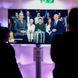 Medienvertreter blicken auf einen Bildschirm, auf dem Olaf Scholz und Alice Weidel, in der ARD-Wahlarena zu sehen sind.