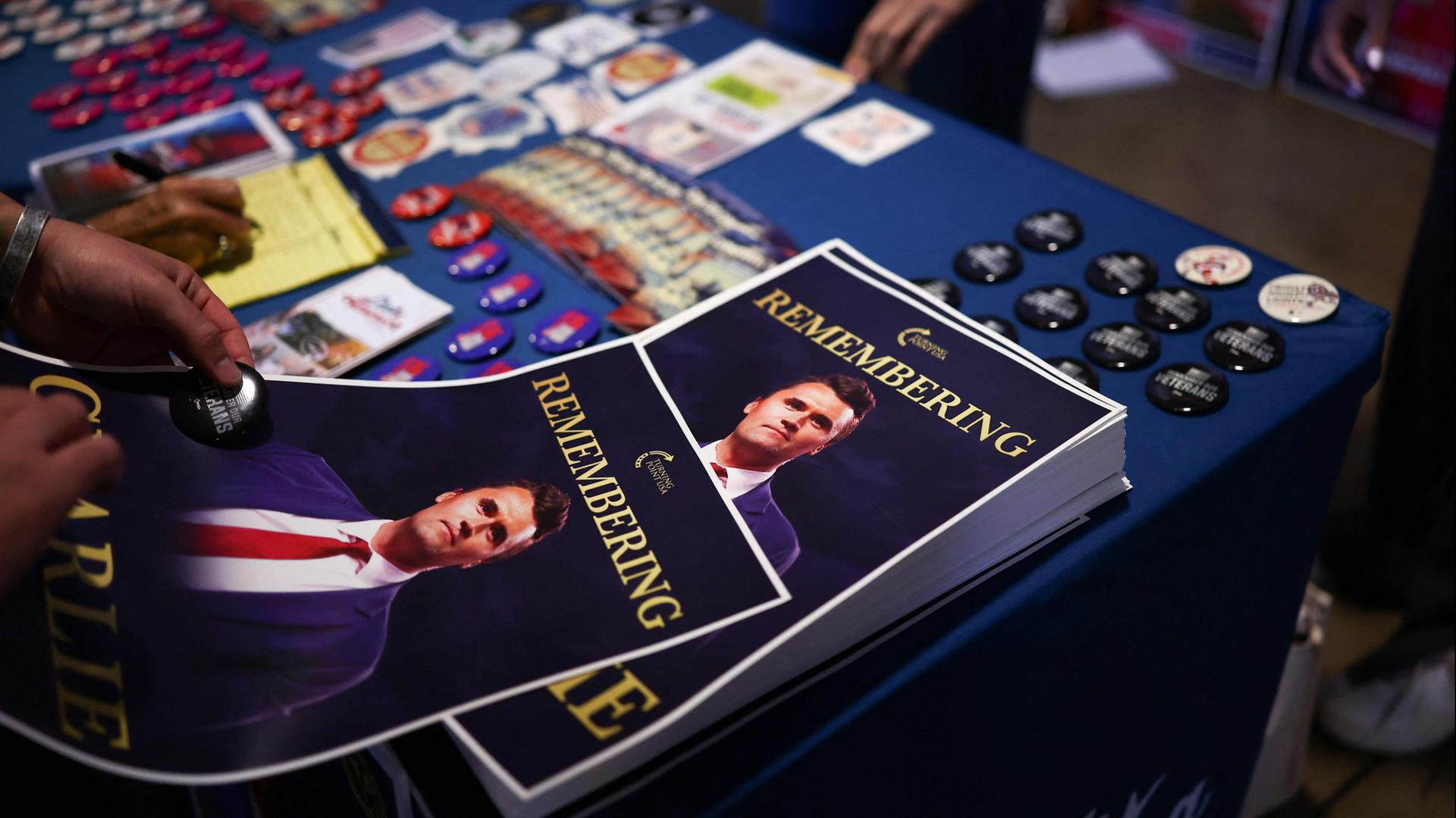 Plakate zur Erinnerung an den getöteten Charlie Kirk liegen auf einem Tisch. | AFP