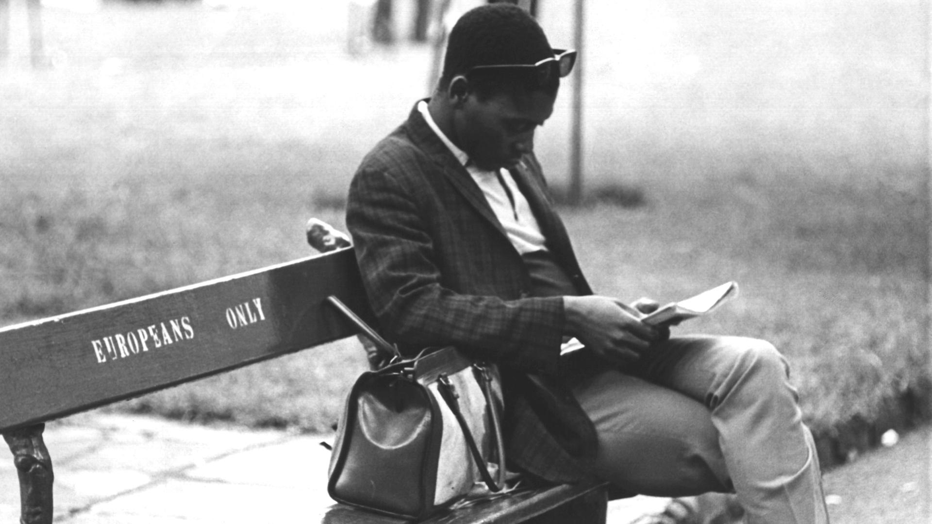 Ein Schwarzer Mann sitzt auf einer Parkbank in Johannesburg, auf der 